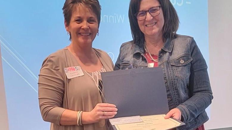 Two people standing and smiling as they hold up a portfolio containing an award